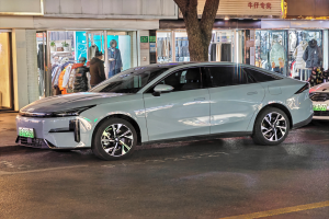 Ein Mitsubishi Lancer EV Elektroauto auf einer Straße bei Nacht geparkt, umgeben von Gebäuden, Geschäften, Schaufensterpuppen mit Kleidern, Schildern mit Text, Lichtern und anderen Gegenständen.