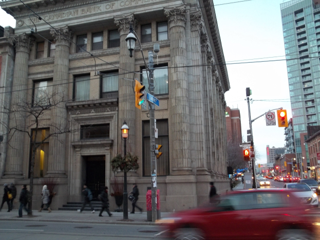 Eine belebte Stadtstraße mit Fahrzeugen, Fußgängern, Gebäuden und verschiedenen städtischen Elementen unter einem sichtbaren Himmel.