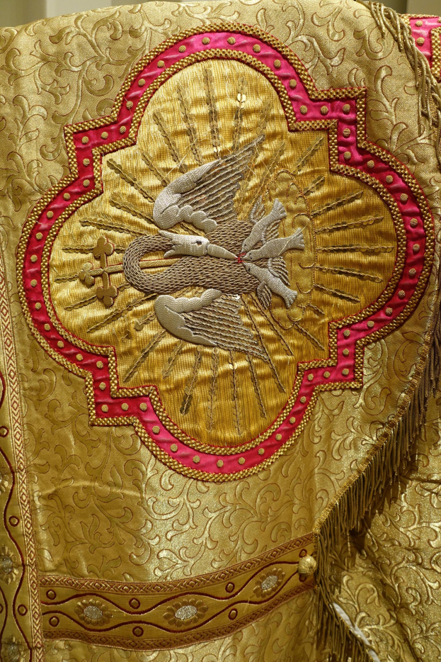 Nahaufnahme eines Priestergewandes mit goldener und roter Stickerei vor einer Wand im Hintergrund.