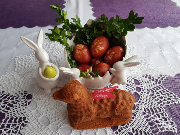 Ein mit einer Decke drapierter Tisch hält eine Schüssel mit bunten Ostereiern mit Osterhasenfiguren darauf.