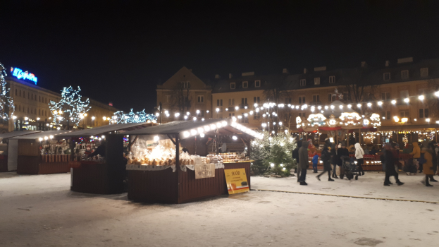 Weihnachtsmarkt-Szene bei Nacht mit Menschen, Buden und schneebedeckter Umgebung.