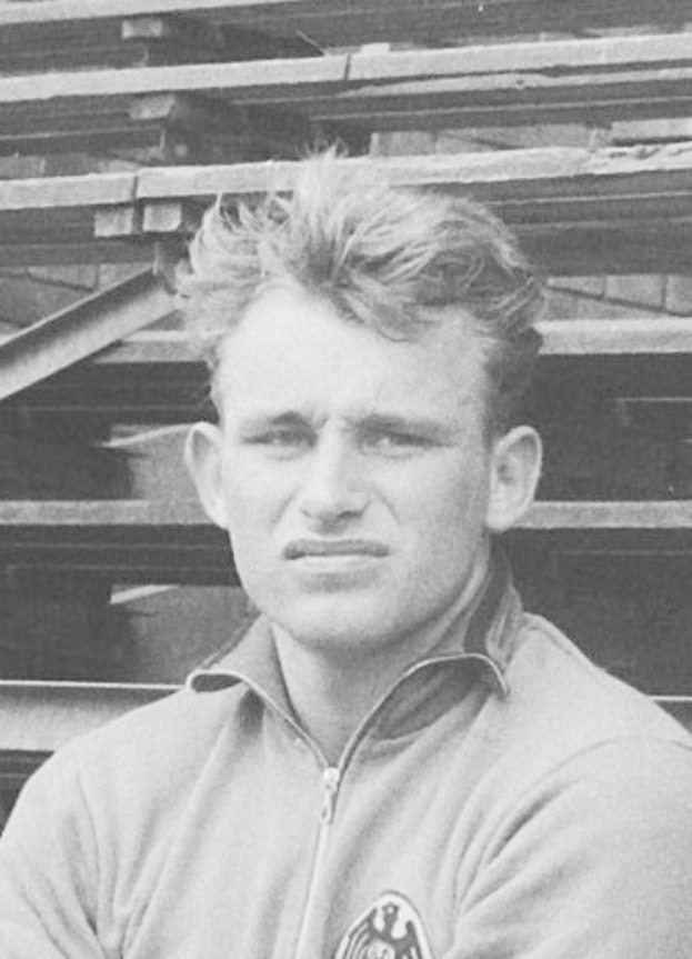 Schwarzes und weißes Foto eines Mannes in einer Jacke, der vor gestapelten Holzplanken steht, der legendäre deutsche Fußballspieler, der im Alter von 89 Jahren starb.