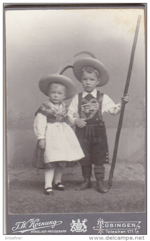 Zwei Kinder in traditioneller bayerischer Tracht, eines hält einen Stock, auf einem Schwarz-Weiß-Foto mit Text unten.