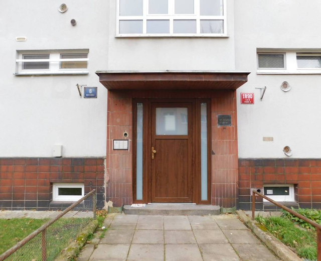 Zweizimmer-Reiheneckhaus mit weißer Fassade, brauner Tür und Fenstern, Metallzaun, Gras, Weg und Brettern an der Wand, zum Verkauf in St Johns Court, St Johns Road, Luton.