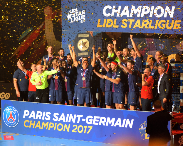 Eine Gruppe von Männern in Medaillen steht auf einem Basketballfeld und hält einen Pokal hoch, mit einer Tafel, die Text und Logos anzeigt, und einem Hintergrundbild, das den Sieg der Paris Saint-Germain Mannschaft in der Lidl Star League feiert.