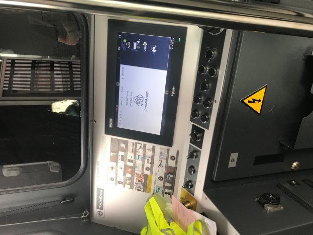 Ein Nahaufnahme eines Geräts mit einem Touchscreen, Knöpfen und einem Glasfenster, das den Innenraum des Fahrzeugs zeigt.