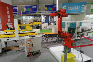 Gruppe von Robotern auf einem Tisch in einer Fabrikumgebung mit Maschinen, Leiterplatten, Kabeln und Menschen im Hintergrund.