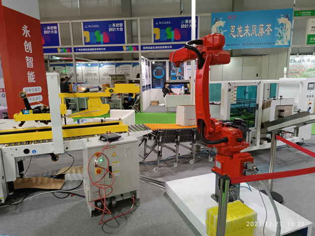 Gruppe von Robotern auf einem Tisch in einer Fabrikumgebung mit Maschinen, Leiterplatten, Kabeln und Menschen im Hintergrund.