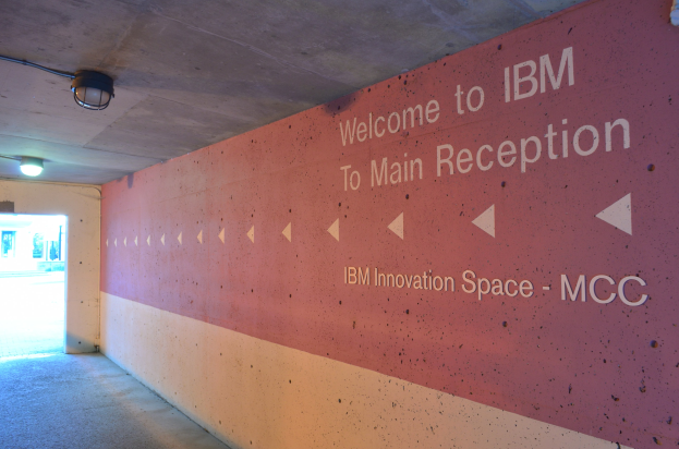 Eine Wand mit der beleuchteten Aufschrift "Willkommen bei IBM" und eine Tür im Hintergrund, die zum IBM Innovation Space MCC führt.