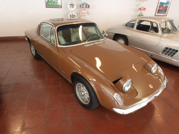 Zwei klassische Autos, ein Ferrari 250 GT und ein Ferrari Dino 246 GT, nebeneinander in einem Raum mit gerahmten Fotos und Tafeln an der Wand dahinter geparkt.