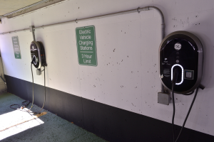 Eine Ladestation für Elektrofahrzeuge in einer Tiefgarage mit zwei an der Wand angebrachten Ladesäulen und Tafeln mit Texten darauf, der Boden ist unten im Bild zu sehen.