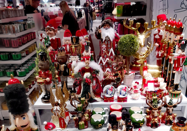 Ladeninneres mit Weihnachtsdekorationen, einschließlich Spielzeug, Tassen und anderen Gegenständen auf Tischen und Regalen, festlicher Beleuchtung und Menschen im Hintergrund.