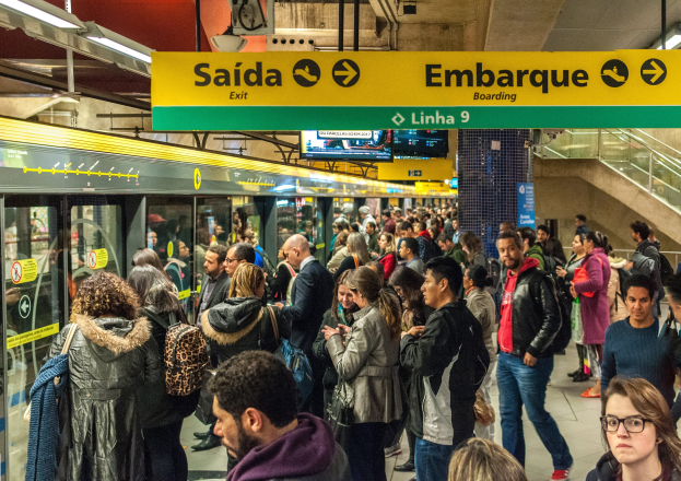 Eine Menschenmenge in einer U-Bahn-Station mit einem Zug auf der linken Seite, beleuchtet von Deckenlampen.