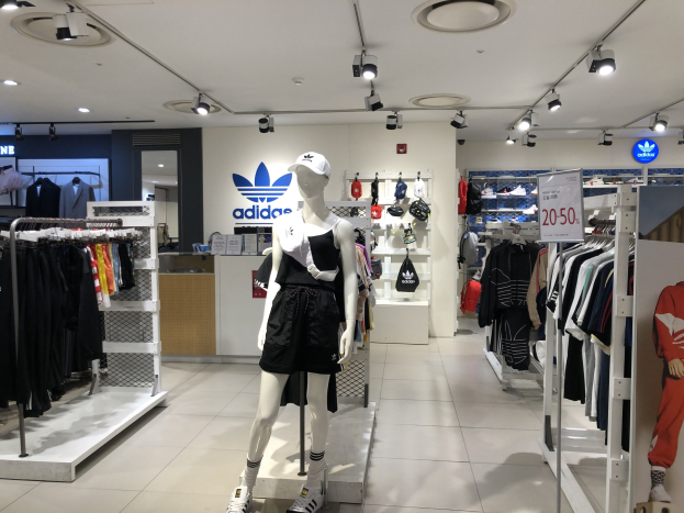 Innenansicht eines Adidas-Geschäfts in Singapur mit Schaufensterpuppen, Kleiderständern, einer Texttafel rechts und Deckenbeleuchtung.