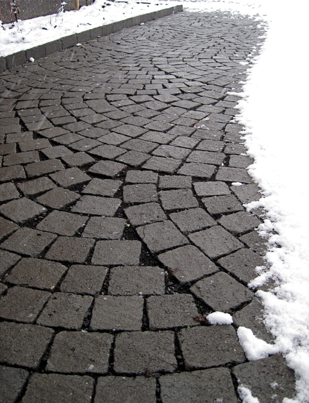 Eine Kopfsteinpflasterstraße mit leichtem Schnee und einem Zaun im Hintergrund.