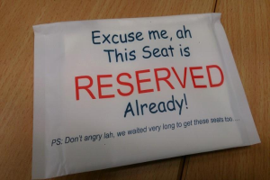 Ein Holztisch mit einem handgeschriebenen Zettel auf Papier, auf dem steht: "Entschuldigung, dieser Sitz ist bereits reserviert."