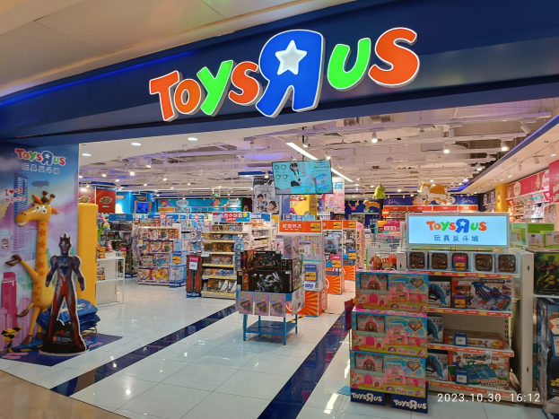 Ein Toys R Us-Laden in einem Einkaufszentrum mit Regalen voller Spielzeug, einem Schild mit Text, Deckenleuchten und einem Wasserzeichen in der rechten unteren Ecke.