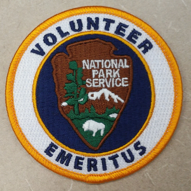 Runder Patch mit blauem Rand und weißem Hintergrund, der den schwarzen Text 'Volunteer National Park Service Emeritus' in der Mitte eines gelben Kreises zeigt.