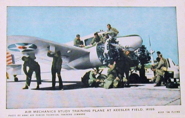 Gruppe von Menschen um ein Trainingsflugzeug auf einer Start- und Landebahn mit einem klaren blauen Himmel, beschriftet mit "Luftmechanikerstudium Trainingsflugzeug auf Keesler Field, Miss."