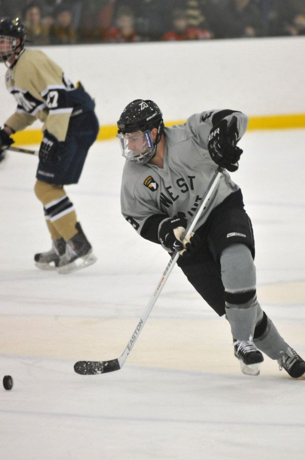 Zwei Männer in Sportkleidung und Helmen spielen Eis hockey auf einem Eisstadion, jeder hält einen Hockeystock, während Zuschauer im Hintergrund zusehen.