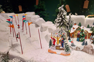 Eine festliche Weihnachtsdorf-Szene mit schneebedeckten Elementen, darunter ein Berg im Hintergrund, unter einem dunklen Himmel, der eine gemütliche Atmosphäre schafft.