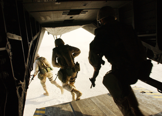 Soldaten in Uniform und Helmen laufen aus einem Flugzeug, jeder trägt ein Gewehr.