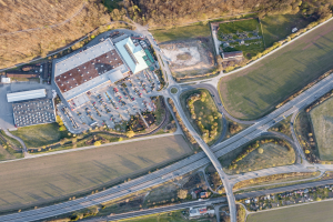 Luftaufnahme eines großen Gebäudes mit einem Firmenlogo, umgeben von Straßen, Fahrzeugen, Bäumen und Gras.