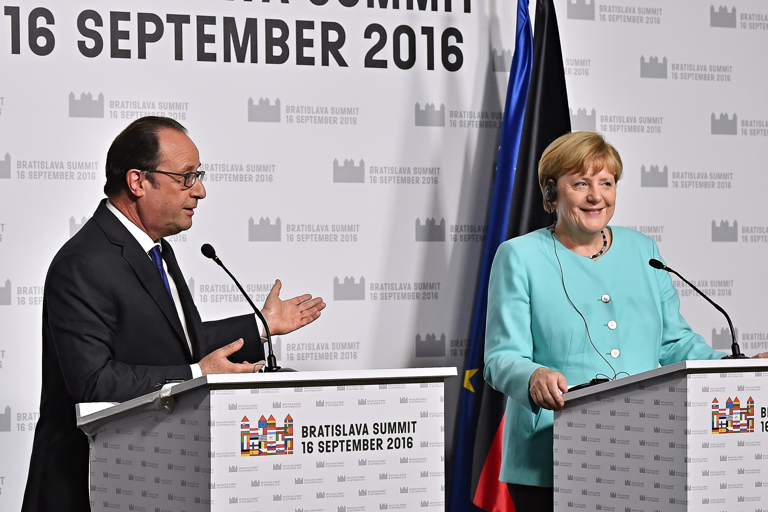 Bundeskanzlerin Angela Merkel und Frankreichs Präsident François Hollande lächeln auf Podien während des Bratislava-Gipfels 2016, mit einem Banner mit der Aufschrift "Bratislava-Gipfel 2016" dahinter.