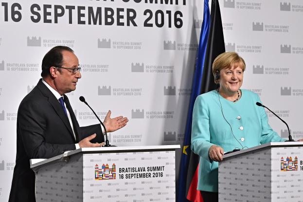 Bundeskanzlerin Angela Merkel und Frankreichs Präsident François Hollande lächeln auf Podien während des Bratislava-Gipfels 2016, mit einem Banner mit der Aufschrift "Bratislava-Gipfel 2016" dahinter.