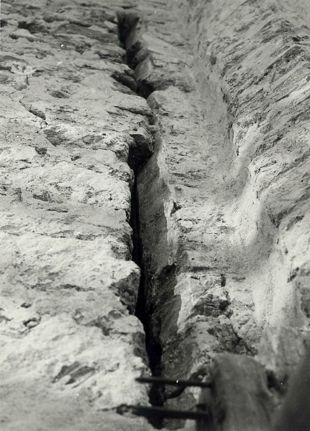 Schwarzes und weißes Foto eines großen Risses im Boden, wahrscheinlich ein Entwässerungsgraben, mit einem Wasserzeichen auf der linken Seite.