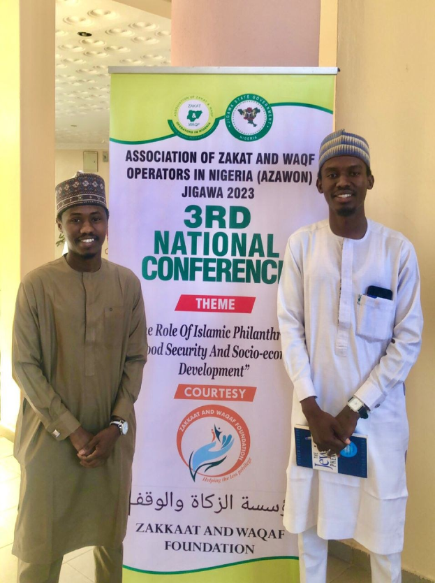 Zwei Männer neben einem Banner "3. Nationalkonferenz" mit einer Säule und Deckenbeleuchtung im Hintergrund.