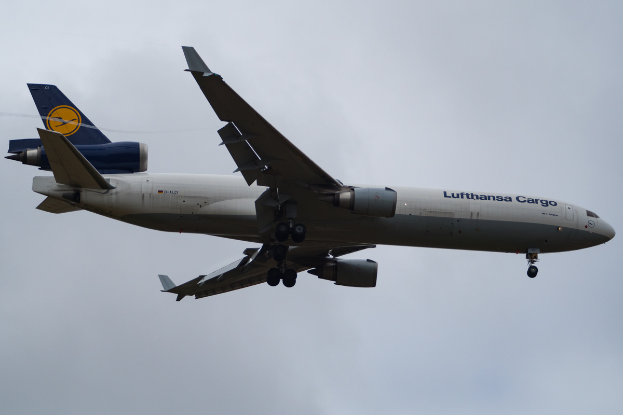 Ein Lufthansa-Cargo-Boeing-777-300ER-Flugzeug im Flug, mit ausgebreiteten Flügeln und aktiven Triebwerken, das durch einen Himmel voller weisser, flauschiger Wolken fliegt.