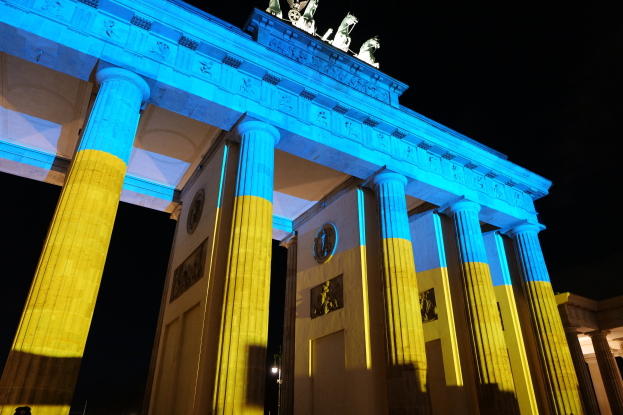 Brandenburger Tor in Berlin in Blau und Gelb beleuchtet, mit Skulpturen gegen einen dunklen Hintergrund
