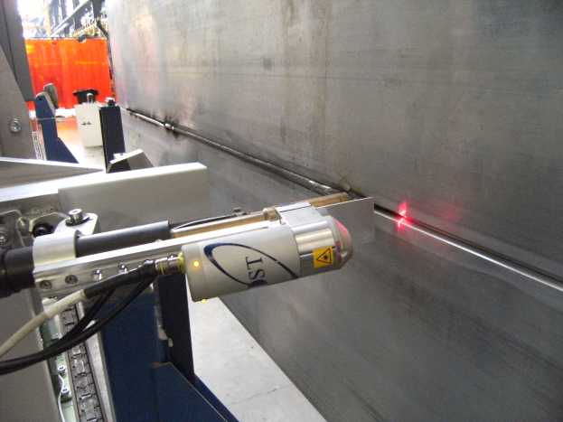 Eine Laser-Schneidemaschine in einer Fabrik, die helles Licht abstrahlt, mit einer Wand auf der rechten Seite und Gegenständen im Hintergrund.