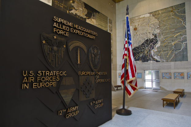 Eintritt zum U.S. Strategic Air Forces Headquarters in Europa mit einer amerikanischen Flagge, Informationsanzeigen, Fotorahmen, Bänken und einer Tür im Hintergrund.