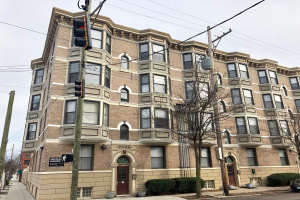 Großes Mietshaus mit der Aufschrift 'Park Apartments for Rent in Chicago, IL' an einer Straßenecke mit Bäumen, Topfpflanzen, Strommasten, einer Ampel, einem Auto und einer bewölkten Himmel.