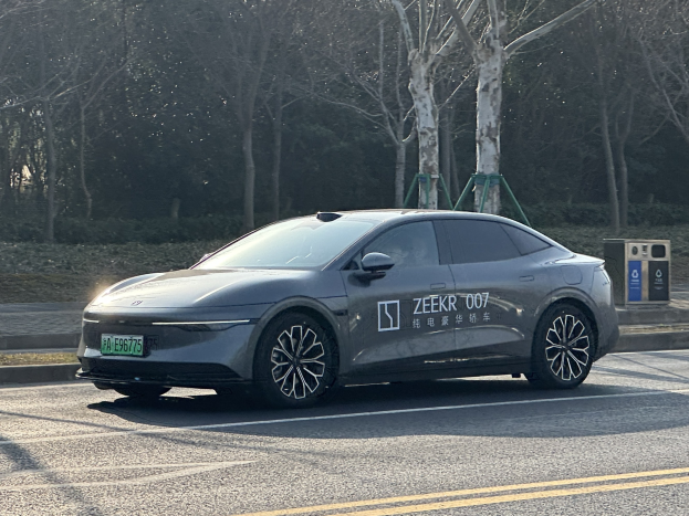 Ein Tesla Model X fährt auf einer Straße in China, mit Bäumen auf beiden Seiten und einem Müllcontainer auf der rechten Seite.