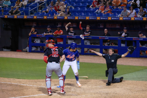 Baseballspieler beim Sliden ins Homeplate mit Zuschauern, Schildern und einem eingezäunten Bereich im Hintergrund.