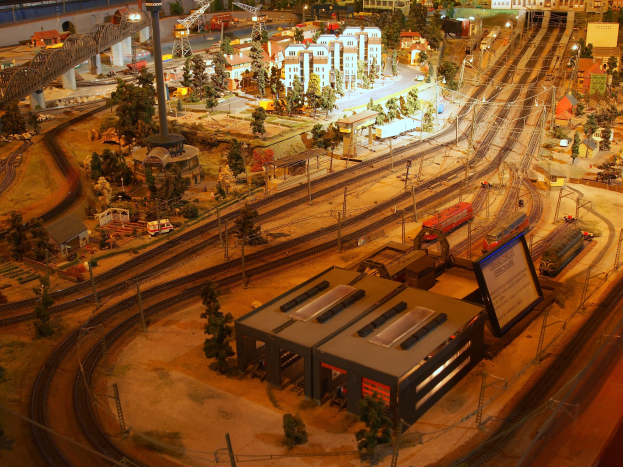 Eine detaillierte Modelleisenbahnausstellung in einem Museum, mit einer Miniaturstadtlandschaft mit Gebäuden, Bäumen, Schienen, Fahrzeugen, Pfählen, Lichtern und anderen Gegenständen.