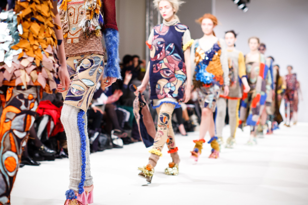 Eine Gruppe Von Frauen, Die Auf Einem Laufsteg In London During Fashion Week Gehen, Mit Sitzenden Zuschauern Und Bühnenbeleuchtung Im Hintergrund.