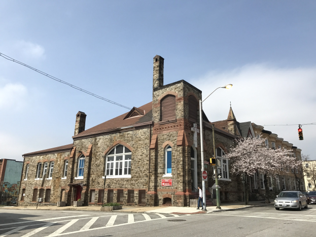 Alte Backsteinkirche First Baptist Church wird an einer Straßenecke mit Fenstern, Laternen, Verkehrsampeln, Schildern, Bäumen und Fahrzeugen renoviert, unter einem bewölkten Himmel.