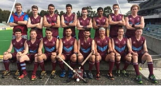 Eine Gruppe von Männern in Sportuniformen steht zusammen auf einem Feld und hält Hockeystöcke in der Hand, während sie ihren Sieg mit einem Stadion und Zuschauern im Hintergrund feiern.
