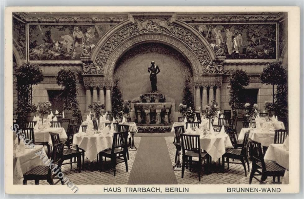 Schwarze und weiße Aufnahme eines alten Berliner Restaurantinnenraums mit Tischen, Stühlen, Blumenvasen, einer Statue, Wandskulpturen, Pflanzen und Text am unteren Rand.