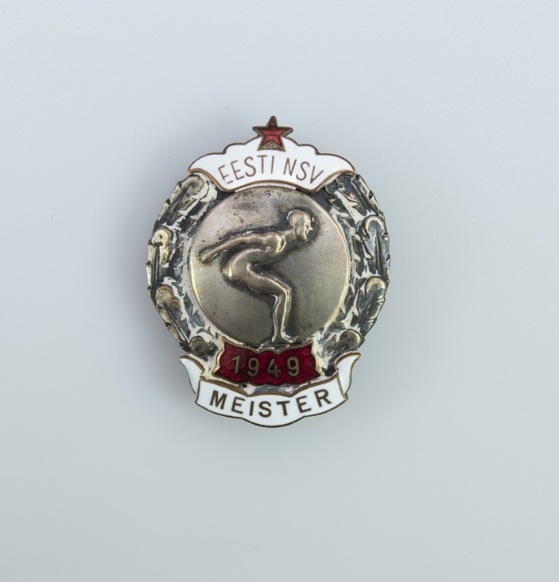Silberner Button mit rotem Stern, Emblem der Olympischen Spiele 1949 in Deutschland, mit Schriftzug in der Mitte auf einem neutralen Hintergrund.