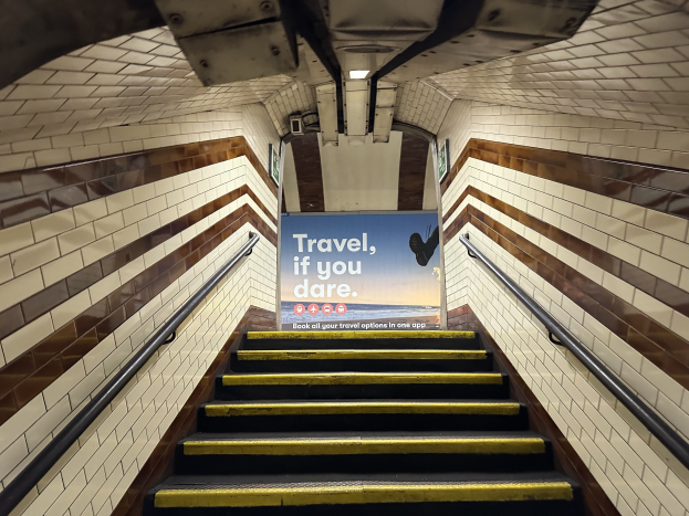 Eine Treppe in einer U-Bahn-Station mit einem Schild "Reise, wenn du wagst" oben, flankiert von Geländern auf beiden Seiten.