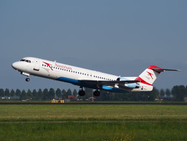 Austrian Airlines Embraer ERJ-190 Flugzeug beim Start am Frankfurter Flughafen, mit grünem Gras, Bäumen, Gebäuden und Himmel im Hintergrund.
