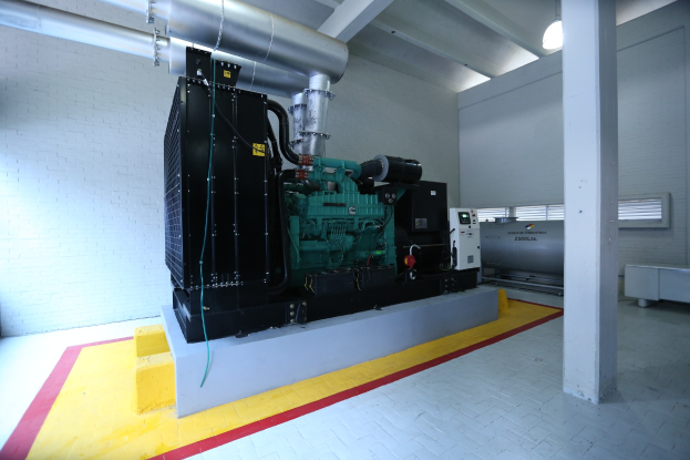 Ein großer Dieselmotor in einem Raum mit einem Boden, einer Säule, einer Wand, Deckenleuchten und anderen Gegenständen.