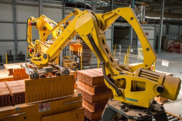 Großes Industriehochregallager mit gestapelten Kisten, Kränen, Zäunen, Pfählen und einer fernen Wand in einer automatisierten Fertigungsumgebung.