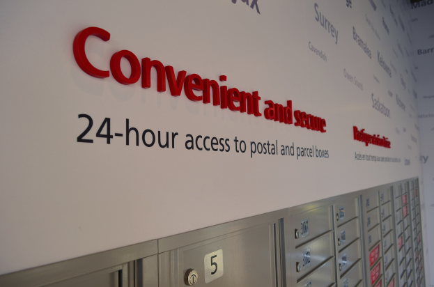 Ein Wandschild mit der Aufschrift "bequem und sicher 24-Stunden-Zugang zu Post- und Paketfächern" über nummerierten Fächern.