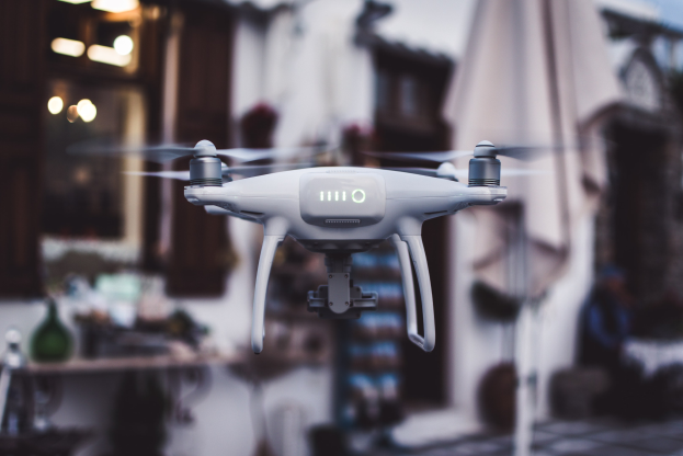 Weiße DJI Phantom 3 Advanced-Drohne, die gegen einen unscharfen Hintergrund von Gebäuden und Lichtern fliegt.